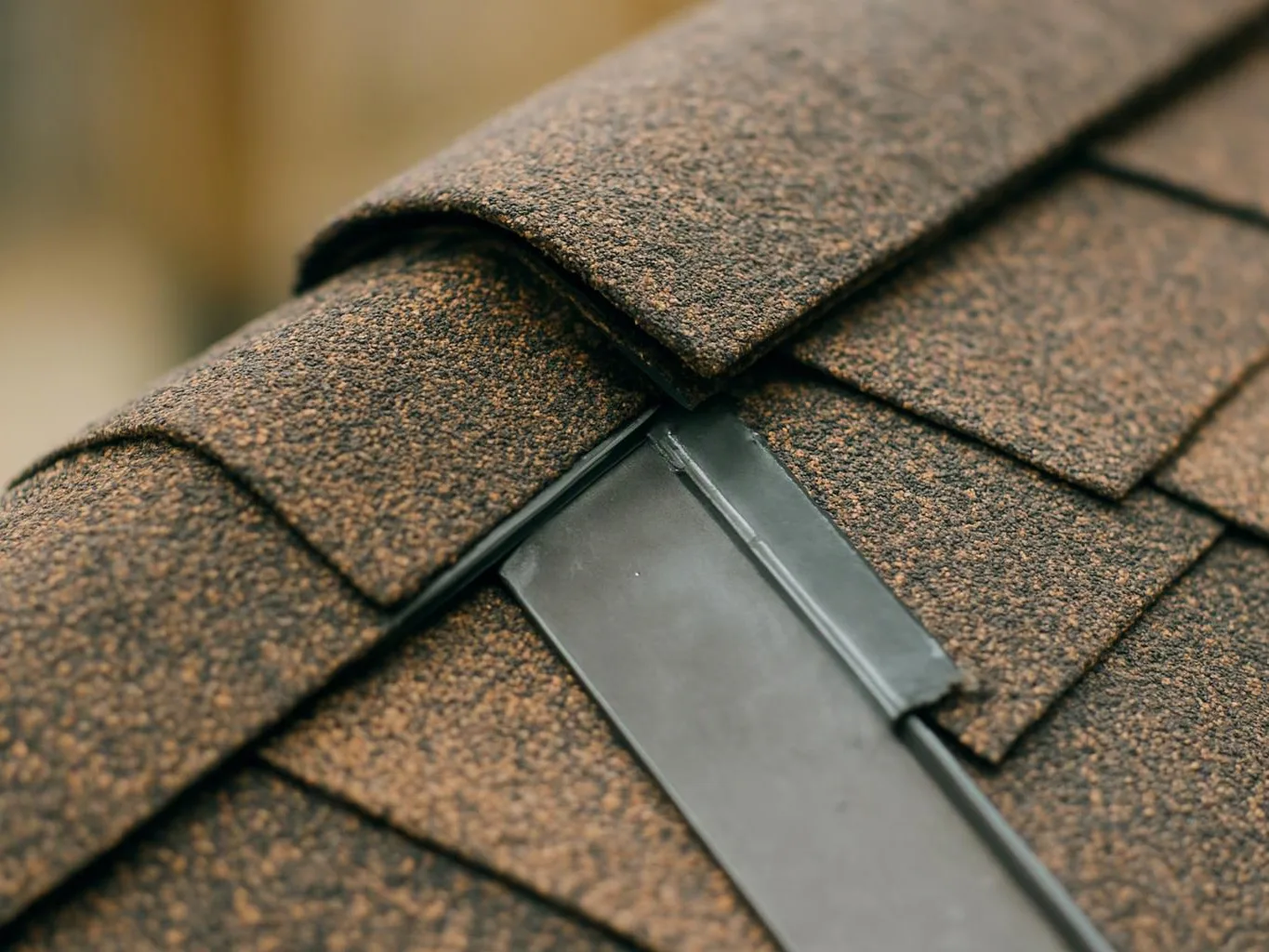 Close-up of brown roof shingles meeting a gray metal flashing seam