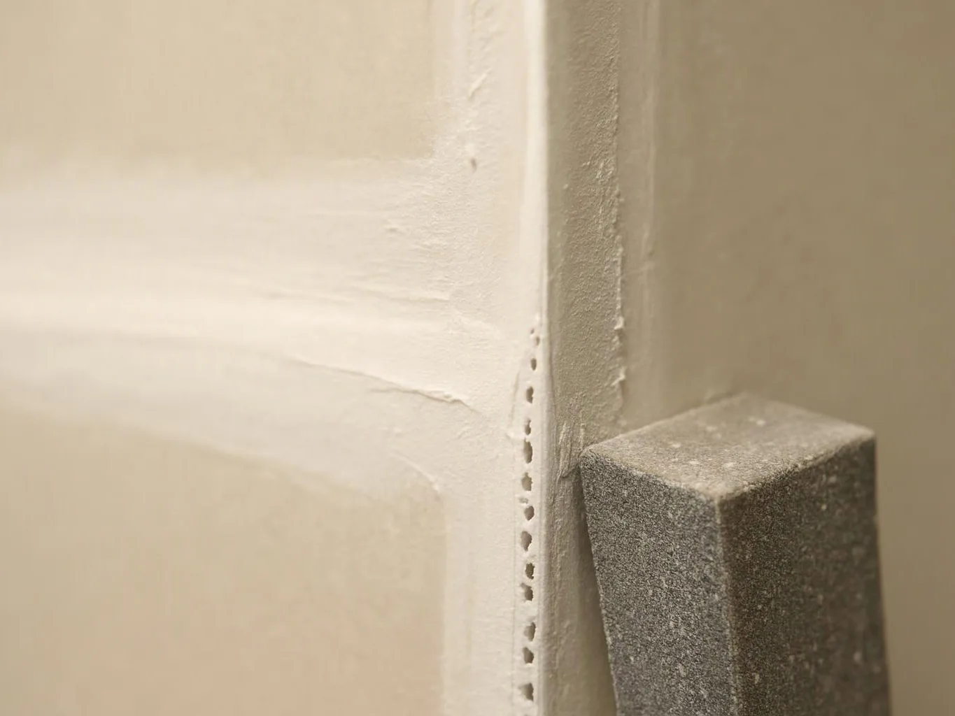 Close-up of a painted wall corner with a rough gray block beside a vertical seam