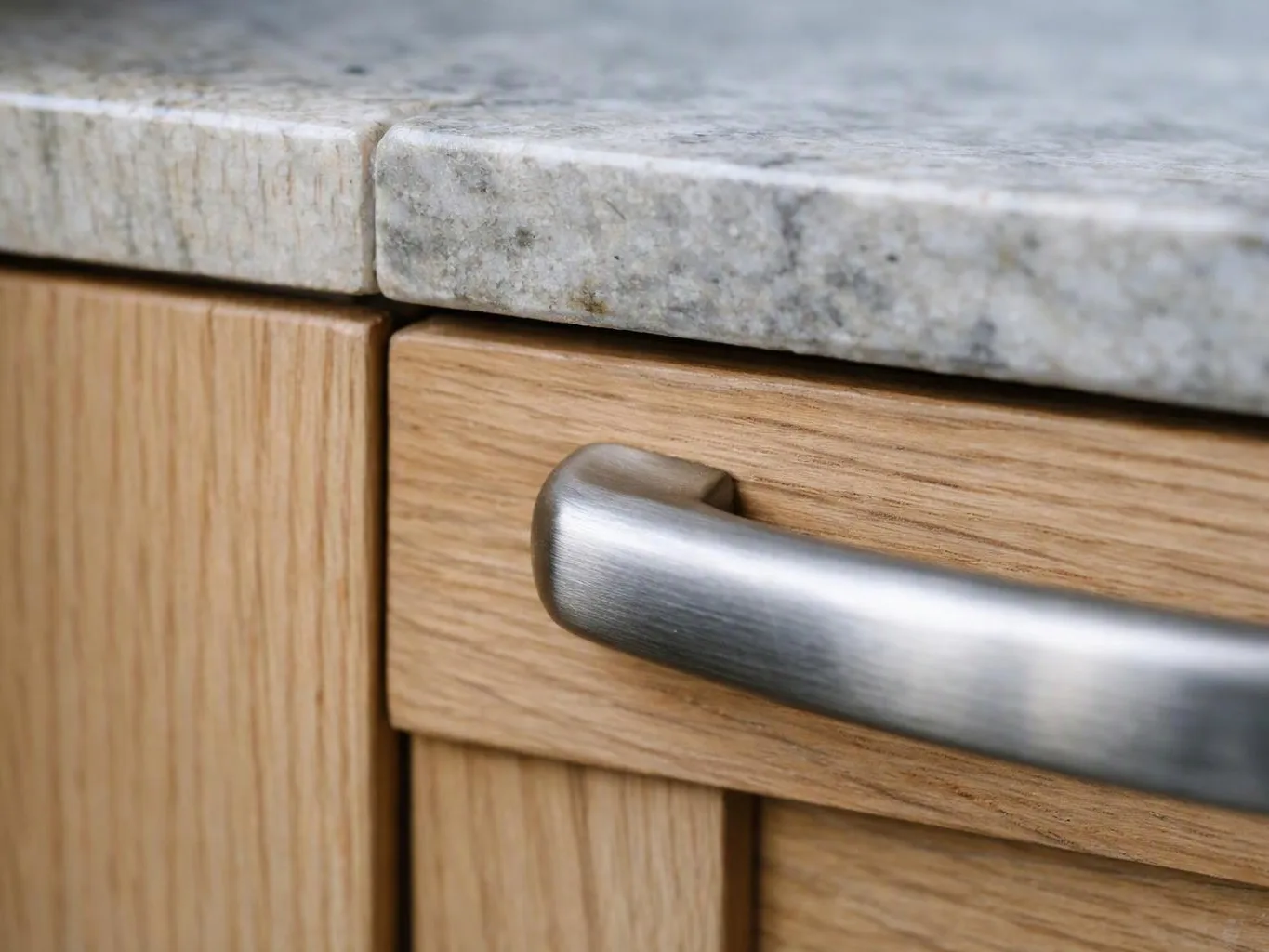 Close-up of a wooden cabinet drawer with a brushed metal handle beneath a gray stone countertop
