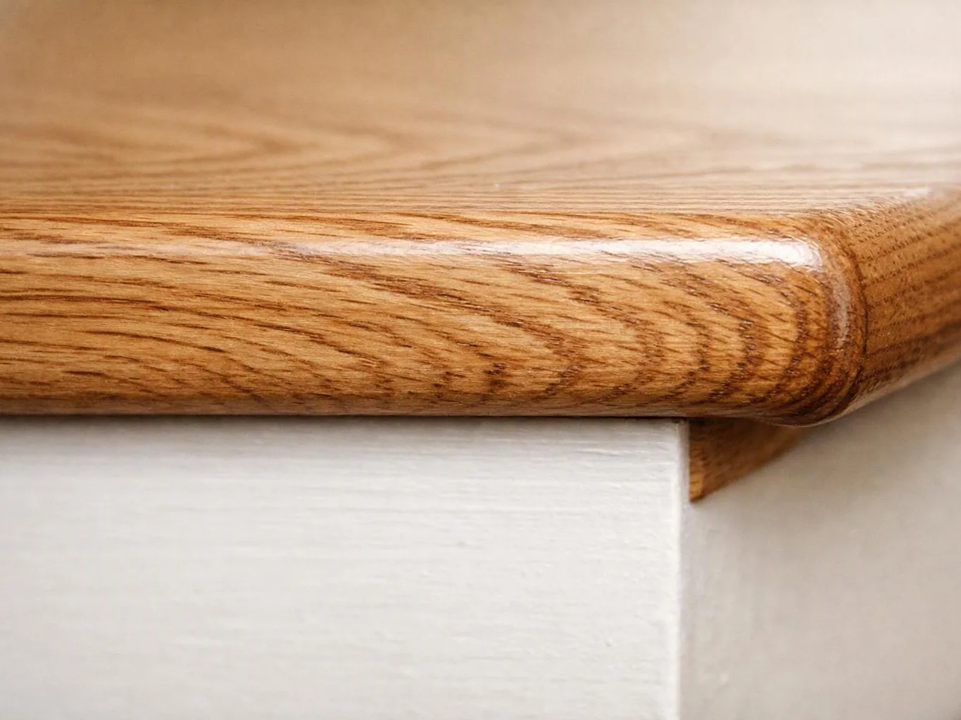 Close-up of a wooden stair tread with a rounded edge above a white riser