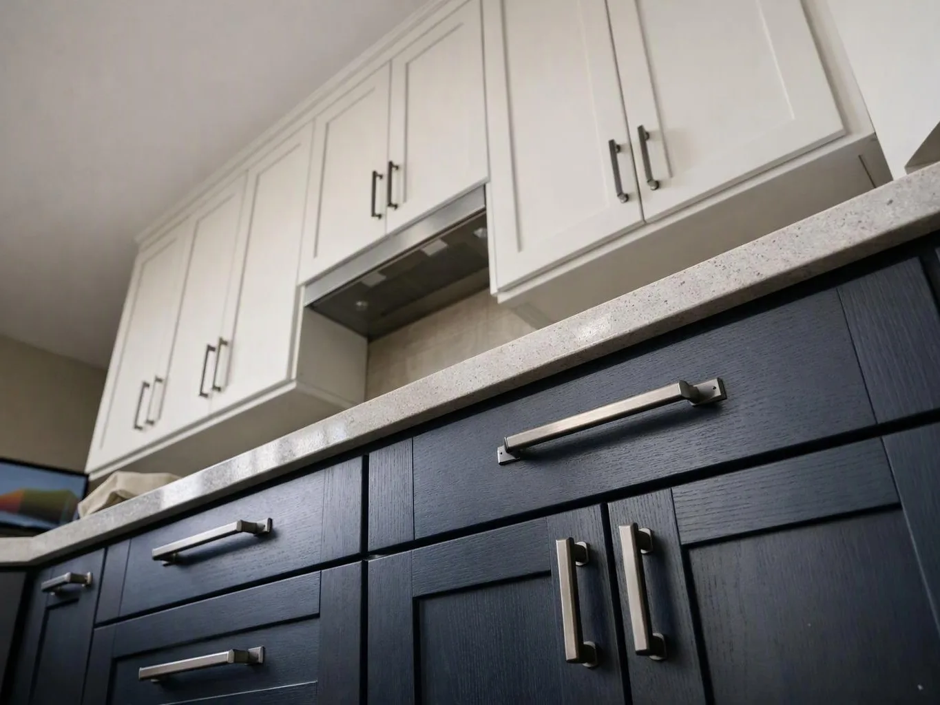 Low-angle view of a modern kitchen with white upper cabinets, dark lower cabinets, and a light countertop