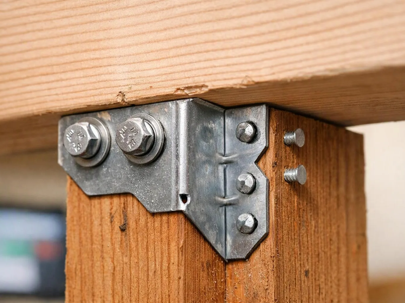 A metal bracket bolts a wooden beam to a larger wooden board underneath