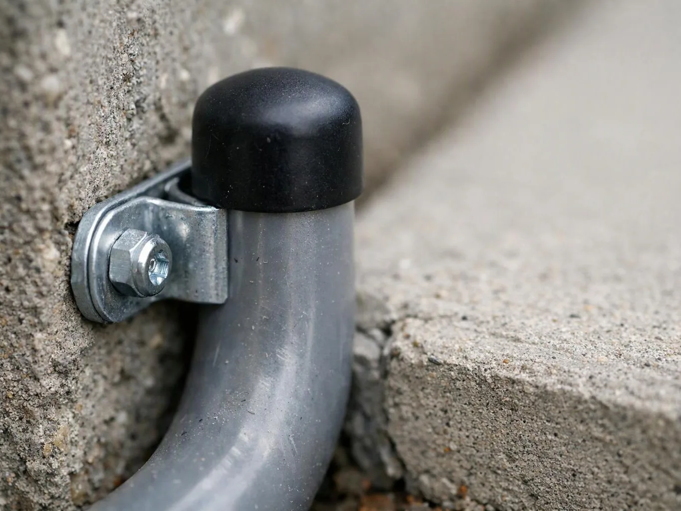 A metal pipe end with a black cap is bolted to rough concrete blocks near a seam