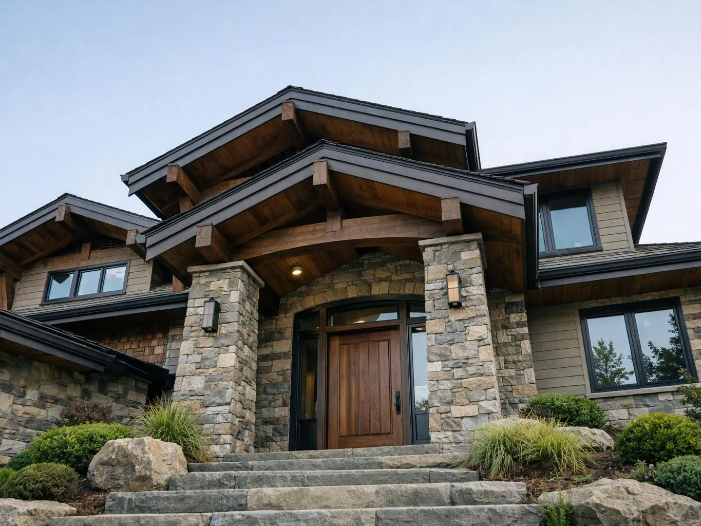 Stone pillars frame a wooden front door on a large house with steep roofs and steps leading up