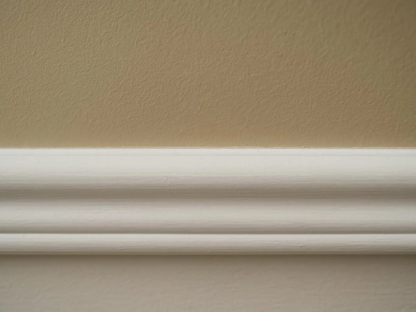A white crown molding runs along a beige textured wall in close-up view